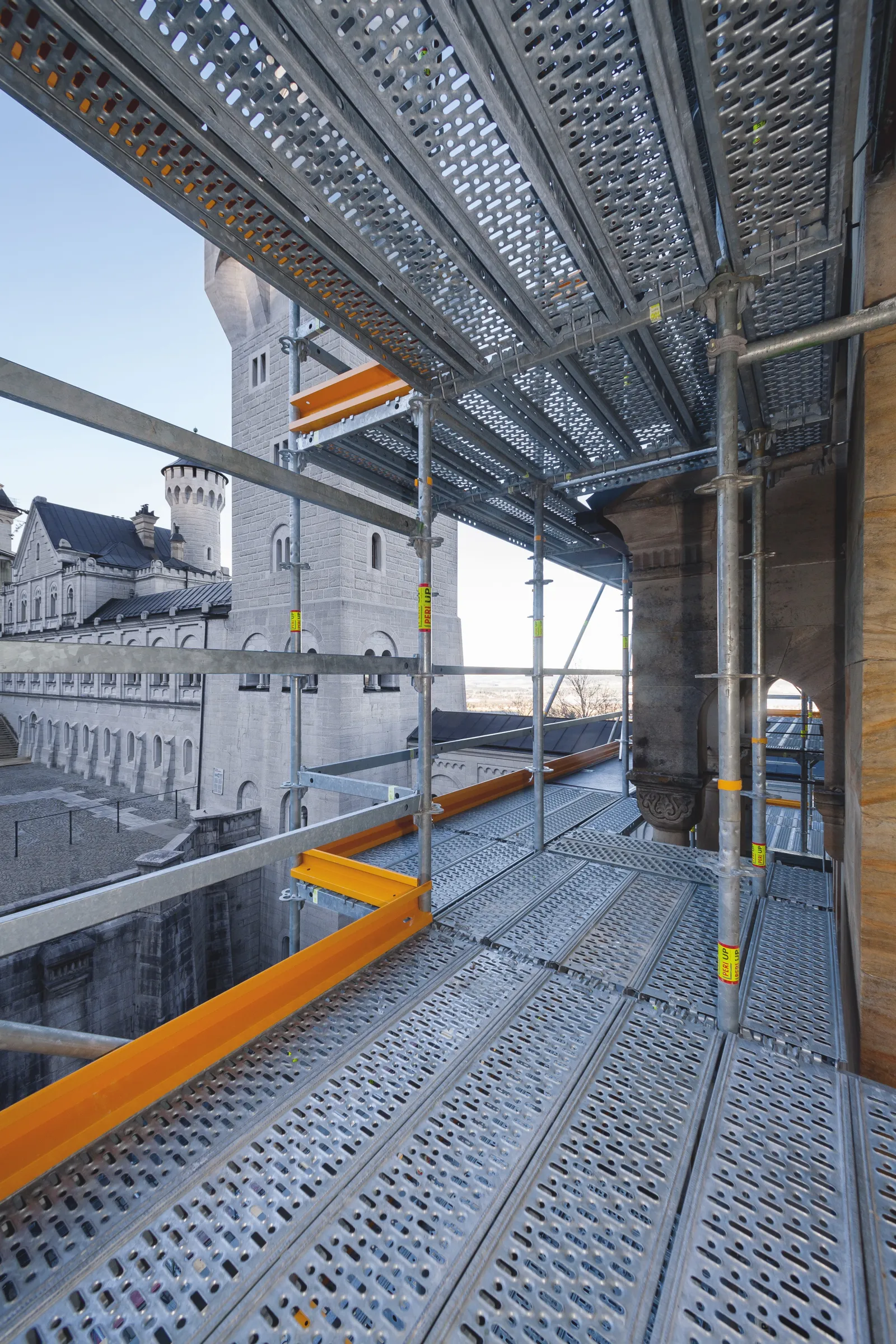 Neuschwansteinin linna näkyy rakennustelineiden läpi, joissa on harmaita metallilevyjä ja oransseja tukia.